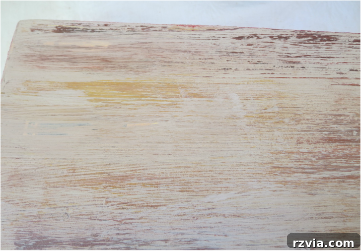Close-up of the laminate box surface after applying multiple layers of chalk paint in various mixed colors, creating a textured, grainy effect to mimic old wood. The brushstrokes are visible, highlighting the depth and distressing technique used.