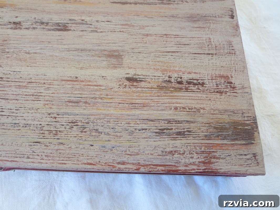 A detailed shot of the laminate box's surface, now expertly painted to resemble old, weathered wood. The texture and varied color tones are clearly visible, showcasing the successful transformation of a smooth laminate into a rustic, antique-like finish.