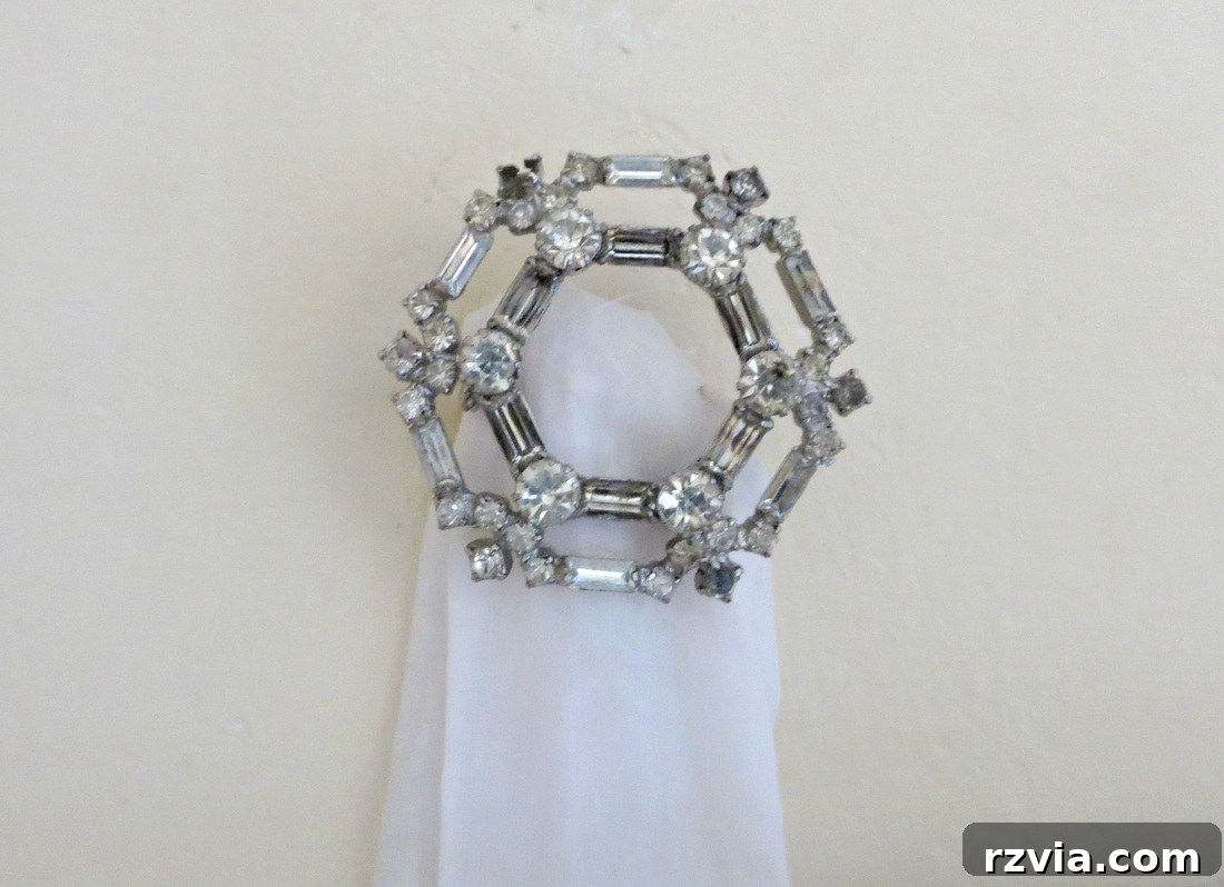 The process of preparing the unique hanging mechanism: an old decorative pin carefully attached to a strip of white fabric, ready to be mounted on the wall for a vertical gallery.