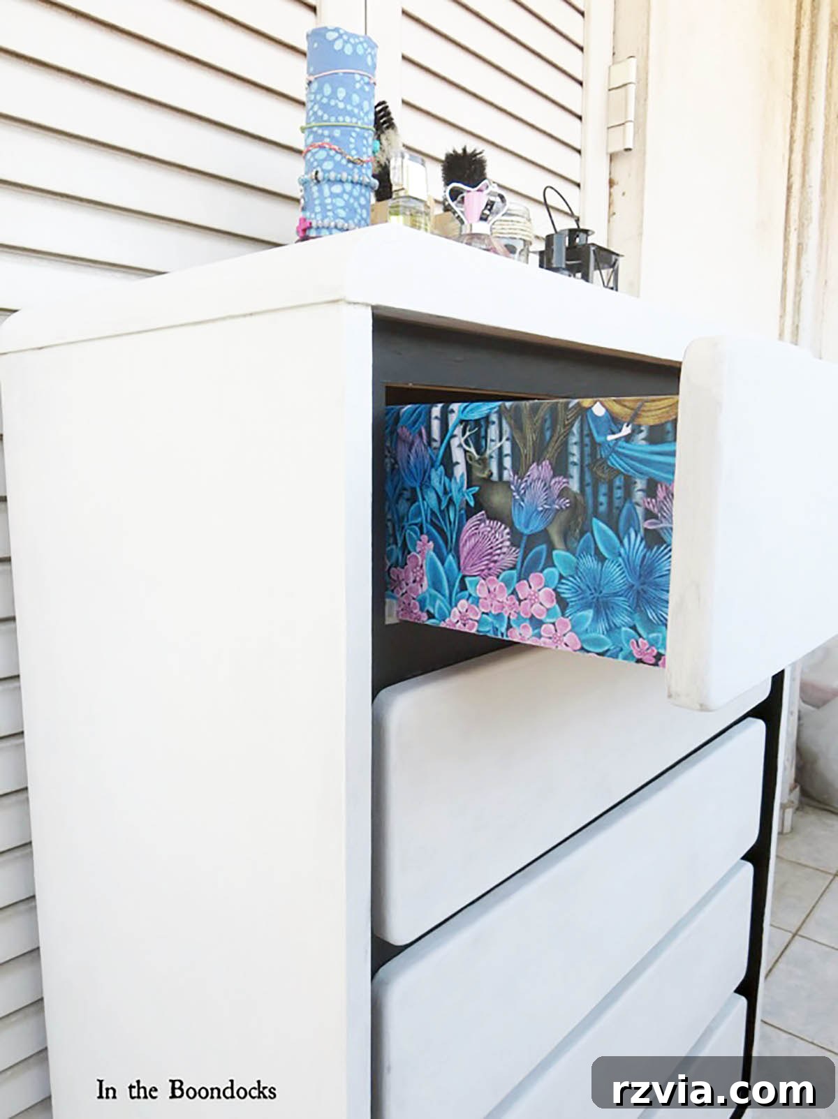 Painted Paper Dresser Revival 2 A side view of the beautifully transformed DIY dresser makeover, showcasing a vibrant blue and pink floral gift wrap decoupaged on the sides of the drawers, complemented by fresh paint.