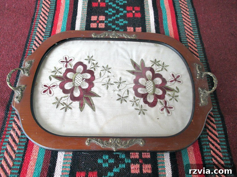Reimagining a Vintage Serving Tray 2 The before image of a dark faux wood rimmed serving tray with handles. The inside has a glass panel covering a vintage embroidered cloth.