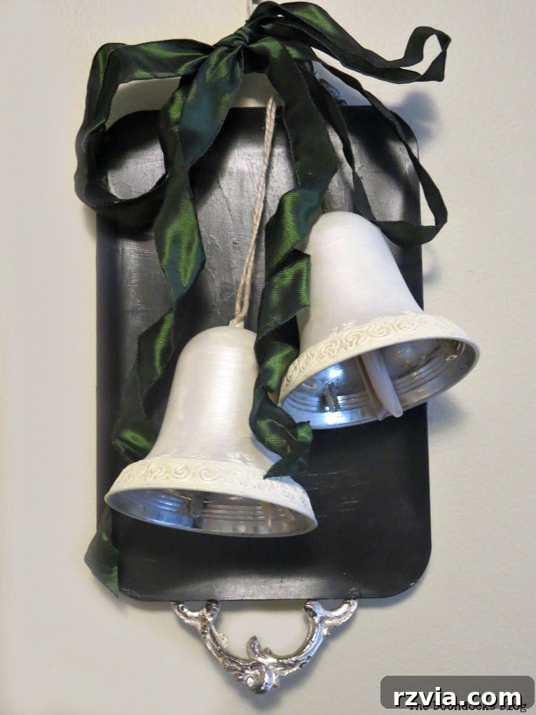 Reimagining a Vintage Serving Tray 11 Metal tray painted black and embelllished with a dark green bow adn two silver bells as holiday wall decor.