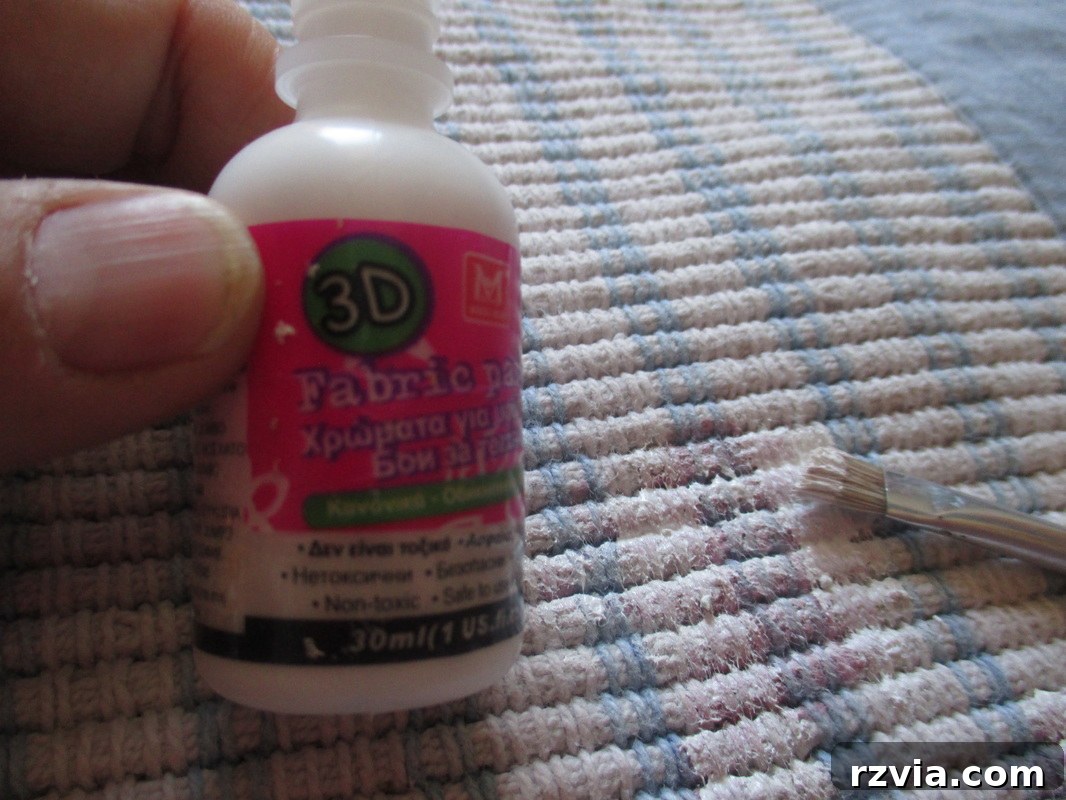 A hand carefully applying white fabric paint over a pink stain on a rug.