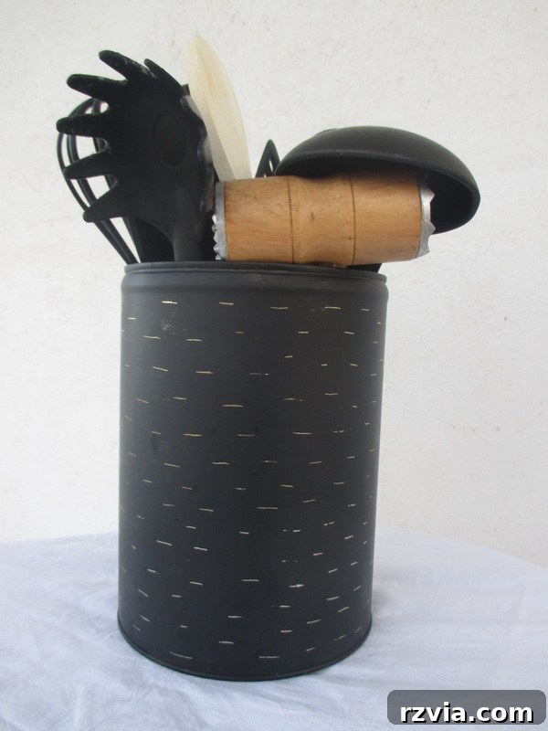 The completed imperfect kitchen utensil holder, an upcycled honey tin, filled with black utensils, showcasing its rustic charm and functionality on a kitchen counter. A perfect example of budget-friendly DIY decor.