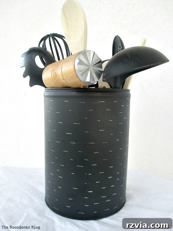 The imperfect kitchen utensil holder, a repurposed honey tin, elegantly holding black utensils, demonstrating how the DIY project seamlessly integrates into a modern rustic kitchen decor scheme. A stylish and functional organization solution.