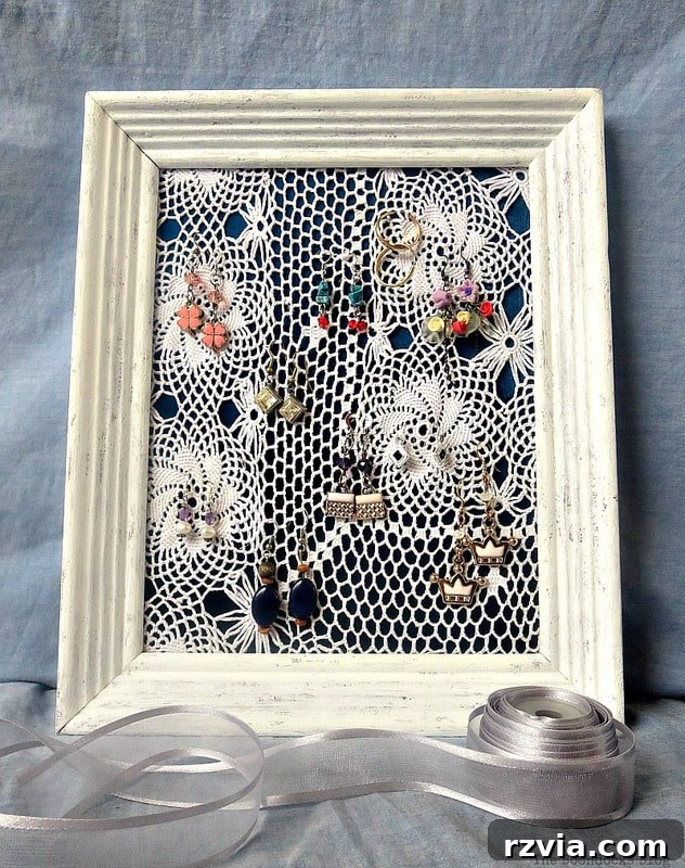 From Discarded to Desired: Upcycling Your Clothes with Style 9 An elegant earring jewelry organizer crafted from a repurposed picture frame, featuring a blue satin blouse as a sophisticated backdrop.