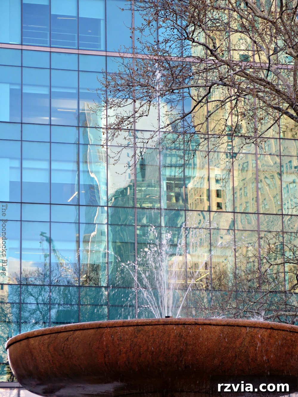 Reflections on the glass facade of a skyscraper with the beautiful water fountain in the foreground, capturing the essence of Bryant Park, New York.