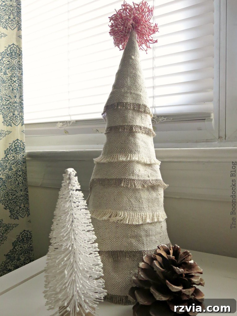 Craft a Charming Fabric Mini Tree from Dollar Store Finds 2 A beautifully handcrafted mini Christmas tree made from fabric scraps, standing proudly beside a smaller white miniature tree and a rustic pine cone, showcasing its unique boho charm.
