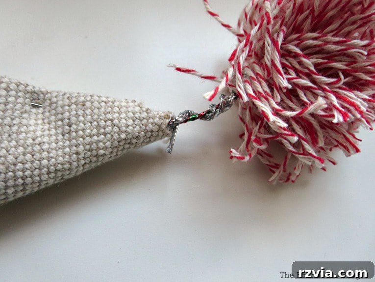 Craft a Charming Fabric Mini Tree from Dollar Store Finds 11 The moment of assembly: the wire stem of the handmade pompom is carefully inserted into the small opening of the fabric cone, securing the topper gracefully to the mini Christmas tree. This step completes the tree's festive look.