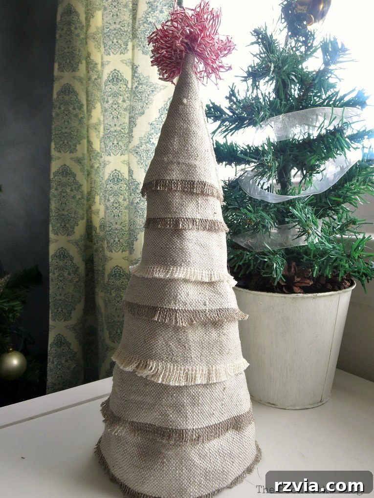 Craft a Charming Fabric Mini Tree from Dollar Store Finds 12 The finished mini Christmas tree, artfully crafted with fabric scraps, stands elegantly in front of a miniature potted evergreen tree. Its textured charm and unique design make it a standout piece of holiday decor.