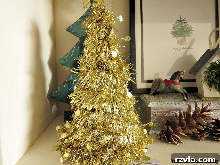 Craft a Charming Fabric Mini Tree from Dollar Store Finds 4 A simple gold tinsel mini tree, freshly purchased from the dollar store, awaits its transformation. It sits alongside a charming miniature horse decoration, a collection of rustic pine cones, and a framed picture, representing its humble beginnings before the DIY magic begins.