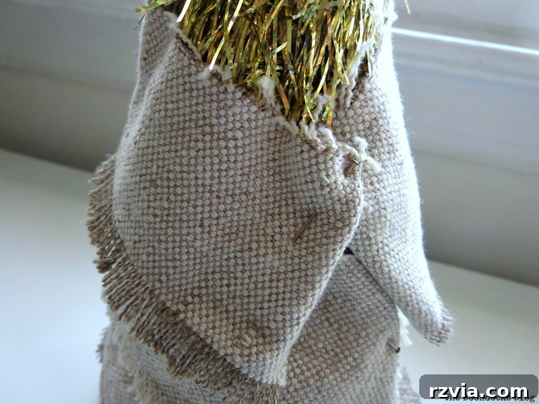 Craft a Charming Fabric Mini Tree from Dollar Store Finds 6 A fabric scrap strip carefully pinned to the back of a tinsel tree, showing the method of attachment and how the fabric begins to conceal the original tree structure. The pin secures the fabric, ensuring a snug fit.