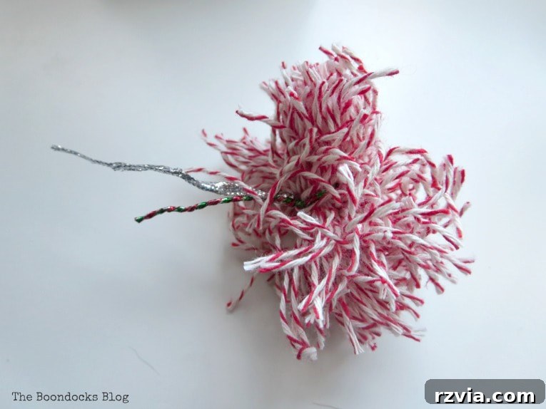 Craft a Charming Fabric Mini Tree from Dollar Store Finds 8 A charming pompom, meticulously crafted from red and white baker's twine, ready to crown the DIY fabric scrap mini Christmas tree. Its vibrant colors add a festive touch.