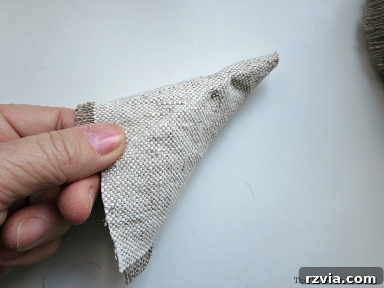 Craft a Charming Fabric Mini Tree from Dollar Store Finds 9 A carefully shaped piece of fabric, formed into a cone, poised to become the finishing cap for the top of the mini Christmas tree. This detail ensures a refined and elegant peak for the craft.