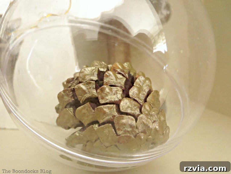 Repurpose Old Decor for Stunning Christmas Vignettes 5 A clear plastic ornament containing a beautifully painted metallic pine cone, demonstrating a creative way to reuse and enhance simple decor items for Christmas.