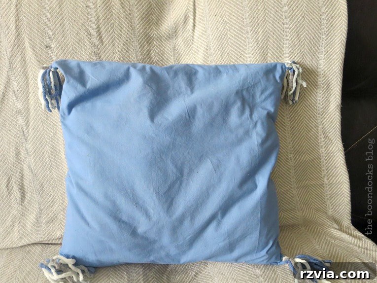 Upcycle Your Fabric Scraps: 5 Easy Pillow Projects 12 Charming blue pillow crafted from a rescued sheet, adorned with playful yarn tassels at the corners.