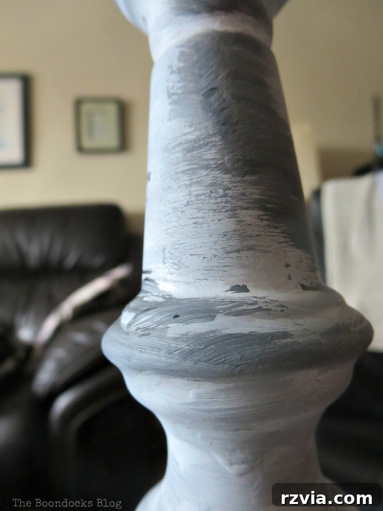 Give Your Lamp Base a High-End Stone Look 5 Applying a layer of medium grey paint onto the white base of the lamp. The brush strokes are deliberate but uneven, allowing patches of white to show through, creating a foundational mottled look. This step is crucial for building the textured stone appearance.