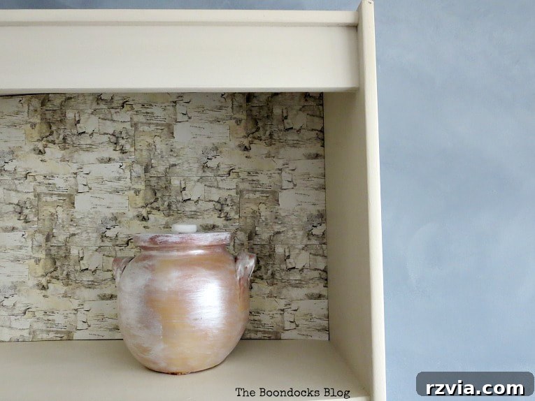 Create Your Own Dreamy Cloud Accent Wall 19 A white bookcase shelf with birch wrapping paper as backing, featuring a painted pot and other decorative items.