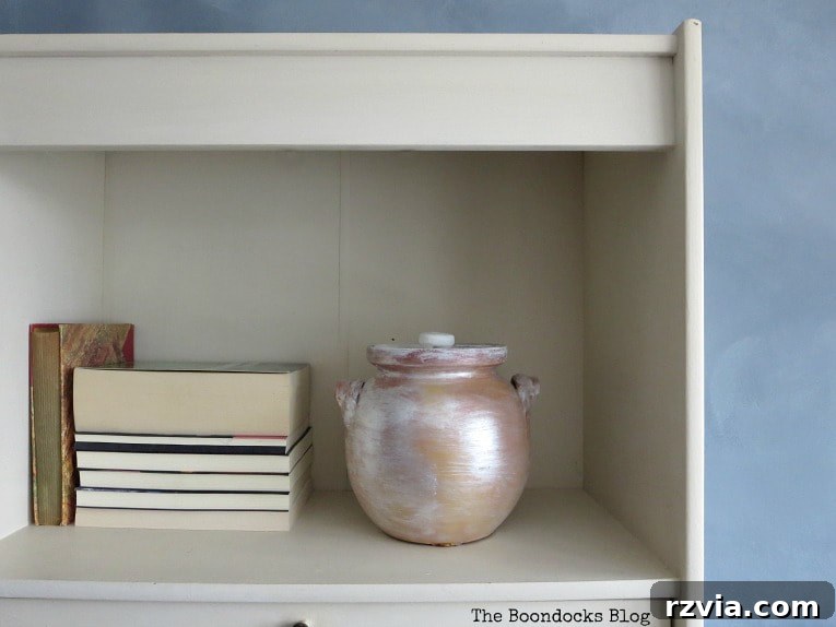 Create Your Own Dreamy Cloud Accent Wall 20 A white bookcase with an off-white backing, adorned with books and a painted pot on the shelf, presenting a cleaner alternative.