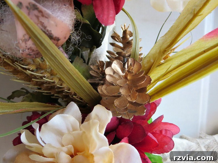 A charming cluster on the wreath featuring pine cones, wheat grass, and faux flowers, creating a rich autumnal composition.
