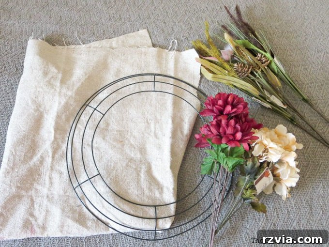Close-up of collected craft materials: wire wreath form, faux flowers, wheat grass, and light fabric, all ready for a DIY fall wreath project.