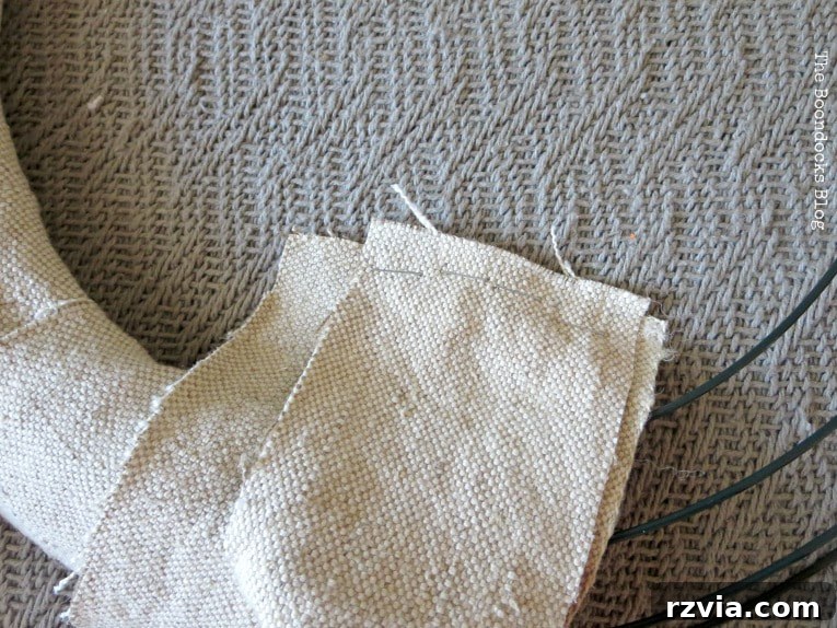 Stapled strips of fabric being wrapped tightly around a wire wreath form, creating a textured base with frayed edges.