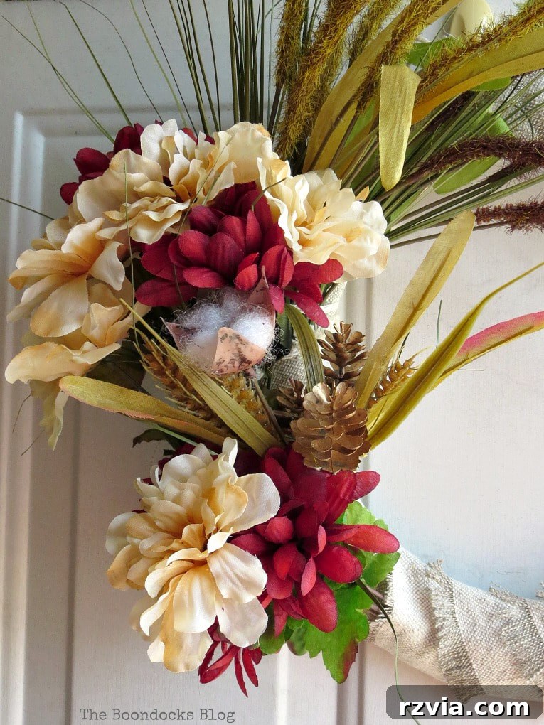Close-up of the mixed faux flowers and pine cones artfully arranged on the rustic fall wreath, highlighting the blend of colors and textures.