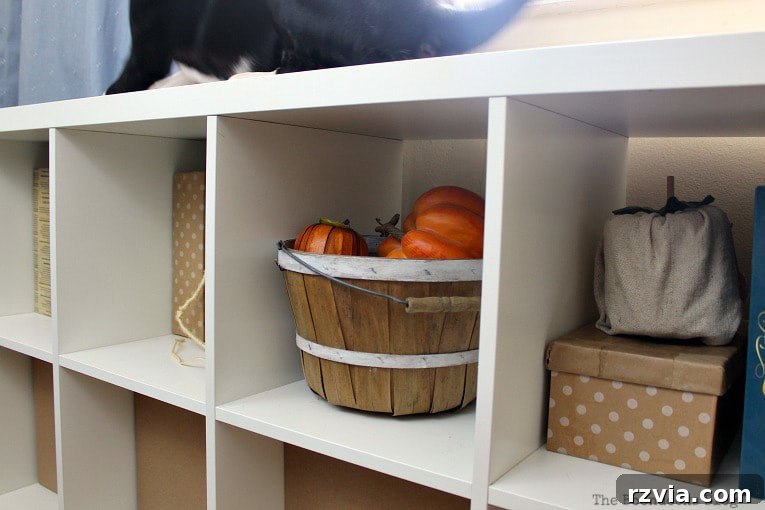 DIY Cardboard Desk Organizer 10 A Kallax storage unit, artfully arranged with a combination of custom-made boxes and a rustic basket, adorned with decorative pumpkins.