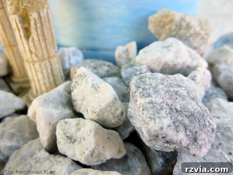 Seaside Style from Salvaged Treasures 11 A close-up view of natural pebbles carefully arranged around the base of the painted planter on a white plate, forming a coastal foundation.
