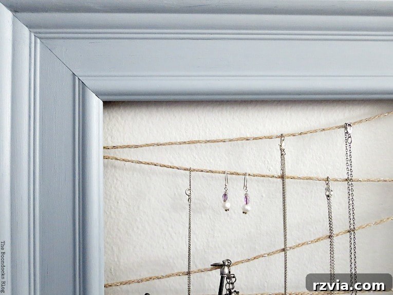 Close-up view of necklaces and hook earrings hanging gracefully on the twine lines of the DIY frame jewelry organizer, highlighting ease of access and organization.