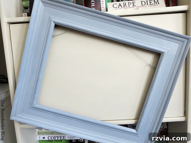 The freshly painted picture frame is hung up to dry, ensuring both coats are fully cured before the next step of the DIY jewelry organizer project.