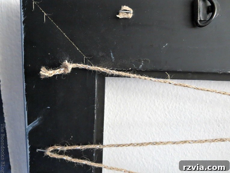 The back of the picture frame with twine securely knotted onto a corner staple, marking the starting point for the zigzag pattern for the jewelry organizer.