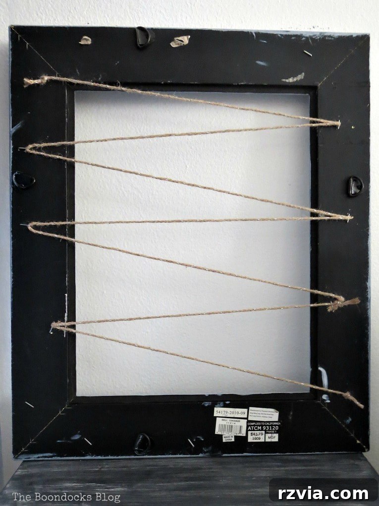 The complete zigzag pattern of twine on the back of the picture frame, ready to hold various jewelry pieces. Staples secure the twine firmly to create hanging rows.