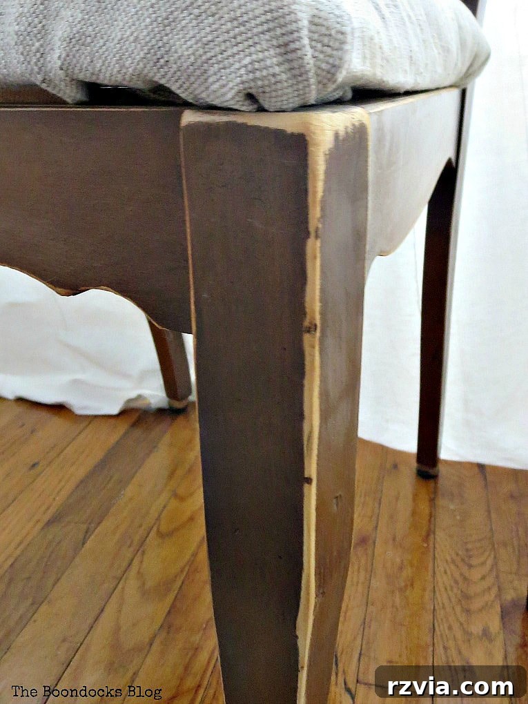 Distressed leg of the finished wood chair, showing intentional wear and natural wood tones, contributing to its rustic charm.