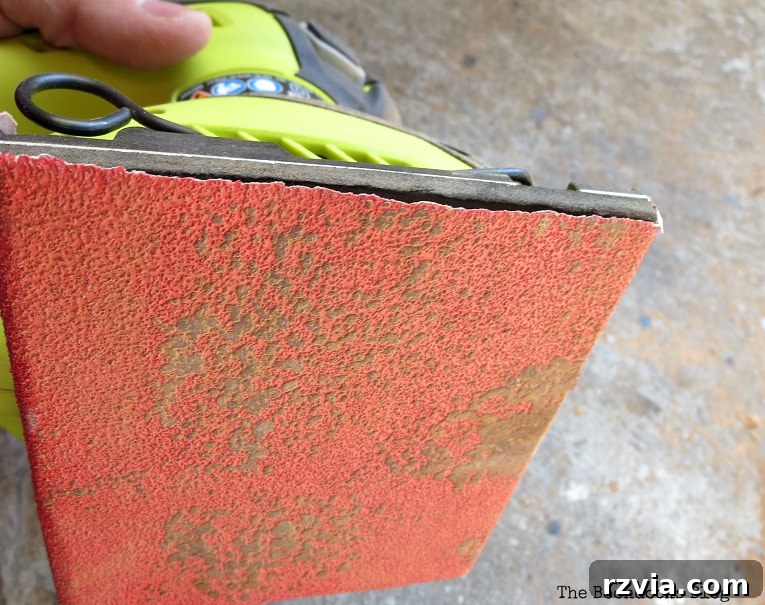 Close-up of sandpaper covered with dark cherry stain from the Mid-Century Modern bench legs, showing intense removal.