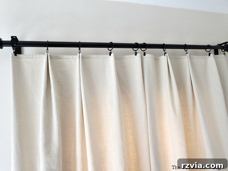 Crafting Elegant Pleated Curtains from Humble Drop Cloths 12 Five clip rings evenly spaced and attached to the top edge of a pleated drop cloth curtain panel.