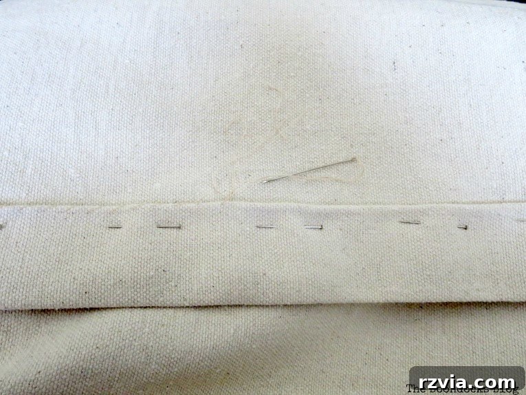 Crafting Elegant Pleated Curtains from Humble Drop Cloths 6 A hand sewing needle stitching a hem on a folded drop cloth edge, demonstrating the crafting process.