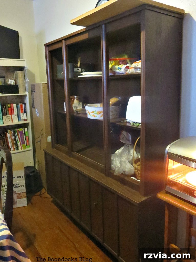 Revitalize Your MCM China Cabinet 3 Before shot of the vintage china cabinet, featuring its original glass doors and open shelving, revealing signs of age and wear.