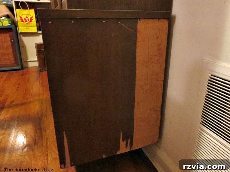 Revitalize Your MCM China Cabinet 9 A disheartening view of the china cabinet's bottom section with large areas of veneer visibly peeling off, revealing the raw wood beneath.