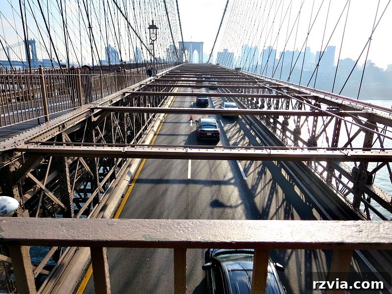 The bustling roadway of the Brooklyn Bridge, with six lanes of modern car traffic flanking the pedestrian path. A Tour of the Astonishing Brooklyn Bridge Walkway.