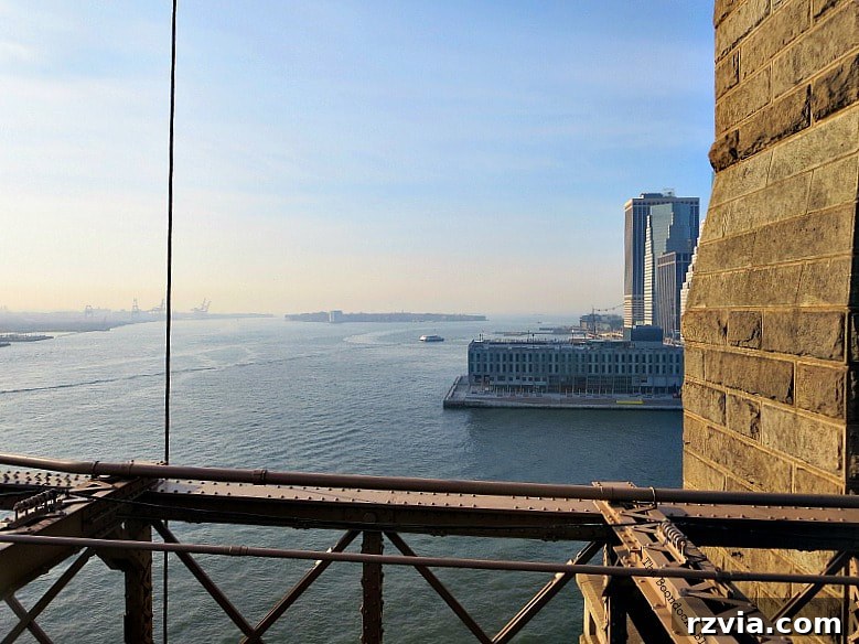 Southern view of the East River from the Brooklyn Bridge, with Governors Island visible in the distance and the Brooklyn shoreline to the left. A Tour of the Astonishing Brooklyn Bridge Walkway.