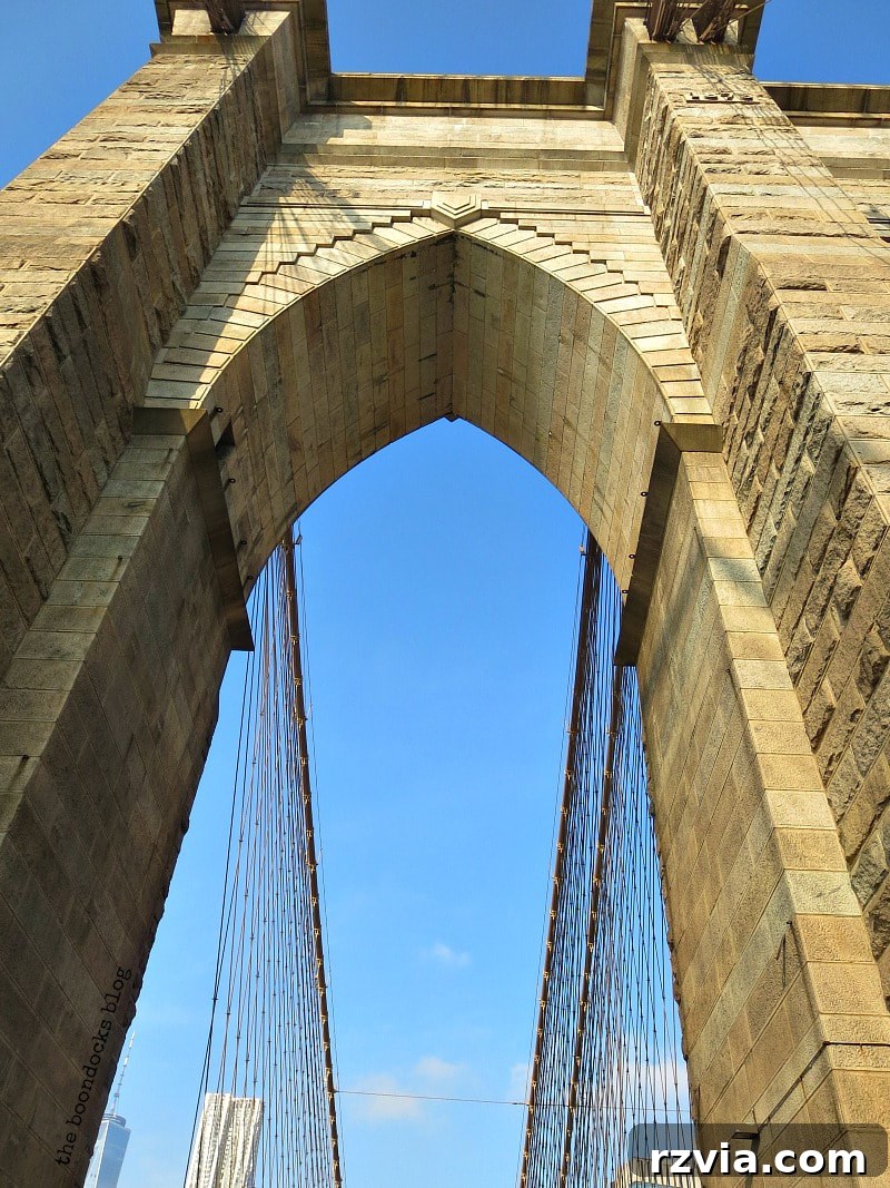 Looking up at the majestic Neo-Gothic Towers of the Brooklyn Bridge, showcasing their impressive height and detailed architecture. A Tour of the Astonishing Brooklyn Bridge Walkway.
