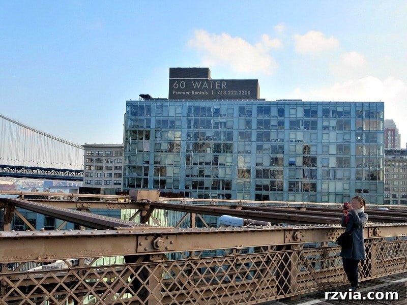 A view from the Brooklyn Bridge walkway towards the trendy DUMBO area of Brooklyn, featuring the distinctive 60 Water Street building. A Tour of the Astonishing Brooklyn Bridge Walkway.