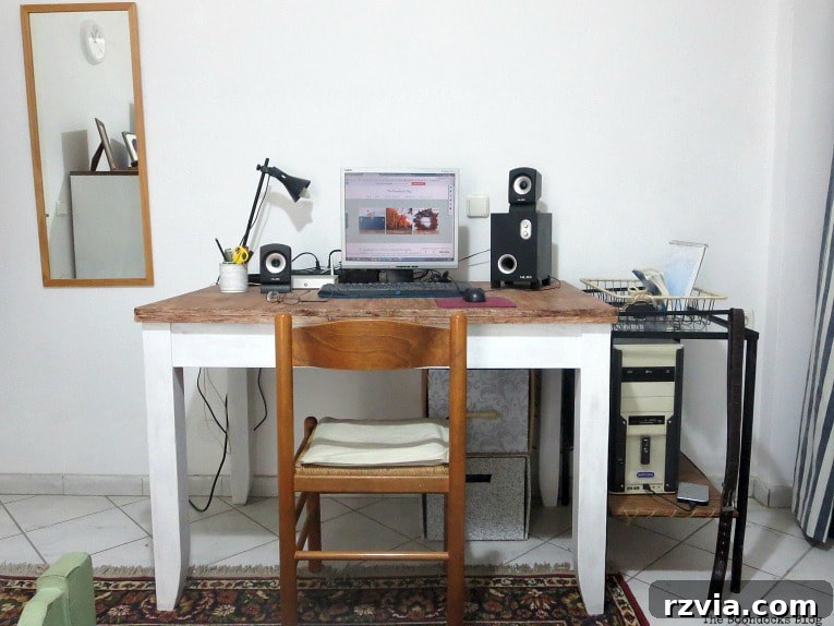 A functional wooden desk is thoughtfully positioned beside a vintage metal table, creating a layered workspace. A decorative wall mirror reflects light and adds depth to the scene.