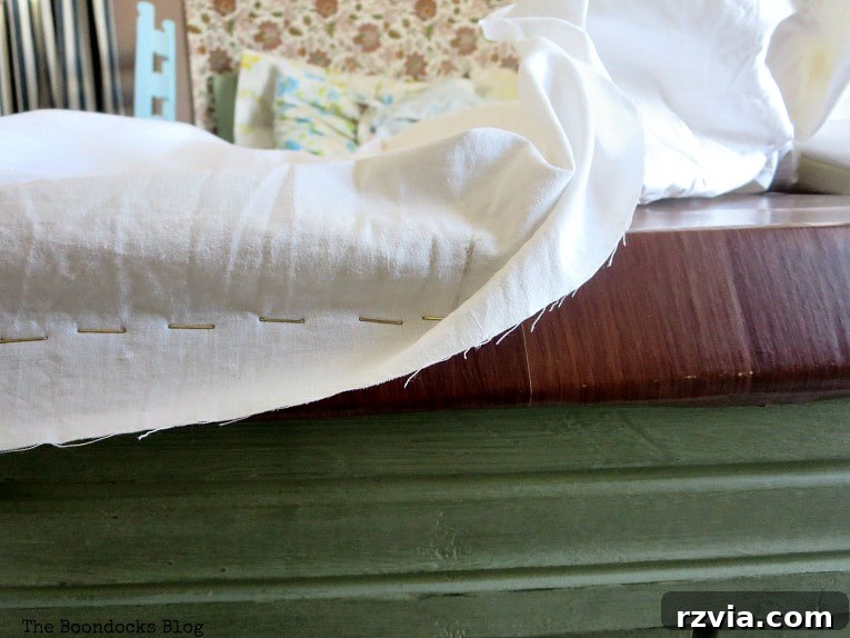 A white flat sheet being carefully stapled onto the cardboard frame, securing the fabric cover around the perimeter of the DIY clothes rack.