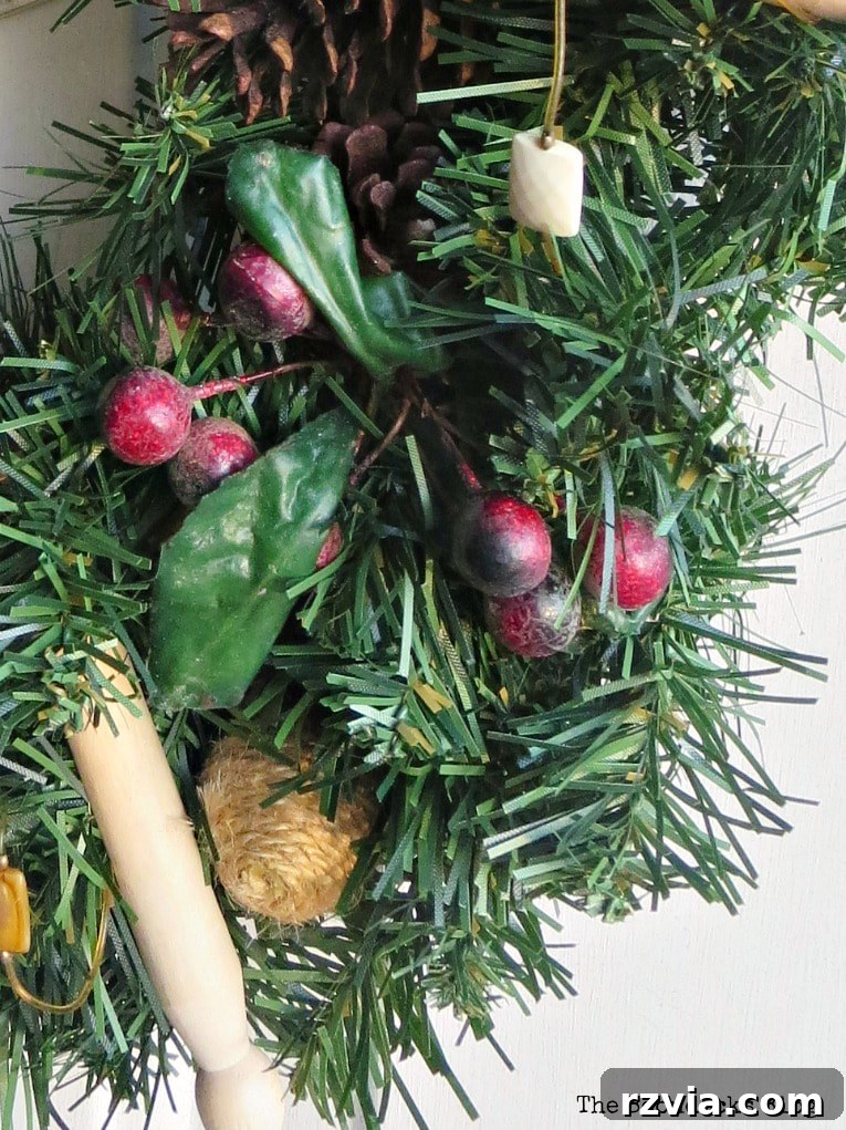 Kolay Rustik Noel Çelengi Yapımı ve 12 Ek Çelenk Fikri 6 Detailed shot of a faux berry sprig being added to the rustic Christmas wreath, enhancing its festive appearance.