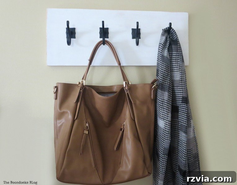 A stylish DIY wooden wall hanger mounted on a wall, showcasing a bag and scarf neatly hanging from the dark gunmetal hooks, adding organization and farmhouse charm.