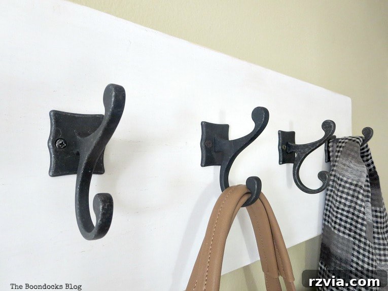 Four sturdy dark gunmetal metal hooks on a white wooden wall hanger, neatly holding a scarf and a bag, demonstrating functional and stylish organization.