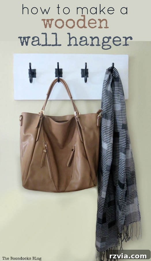 A beautifully completed DIY coat rack with a white board and dark gunmetal hooks, elegantly adorned with a brown leather purse and a grey checkered scarf, displayed on a beige wall.