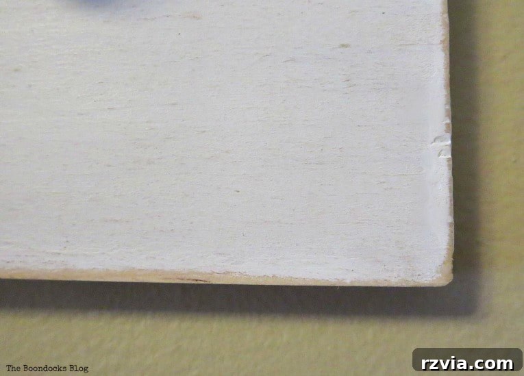 Close-up of a hand sanding the edges of a painted wooden board for a DIY wall hanger. This step ensures a smooth finish and can add a distressed look.